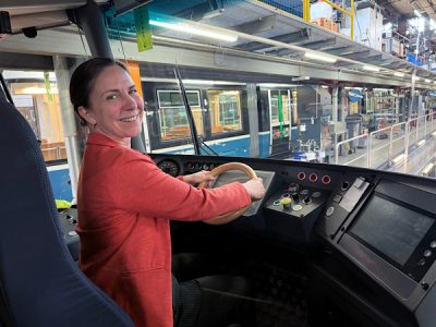 Eine Frau in Orange Jacke im Führerstand vom Cobra Trams in Zürich